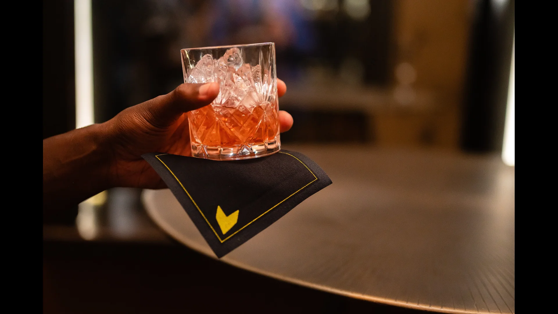A person holding a cocktail with a custom coaster featuring the Gainbridge logo.