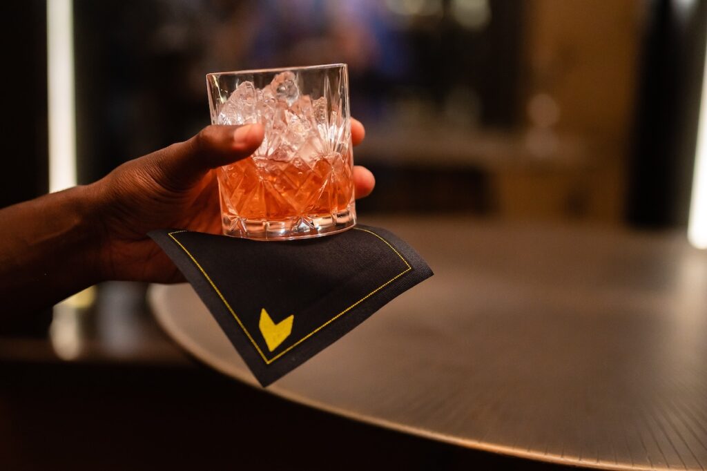 A cocktail glass on a branded napkin — a study in taste and attention.